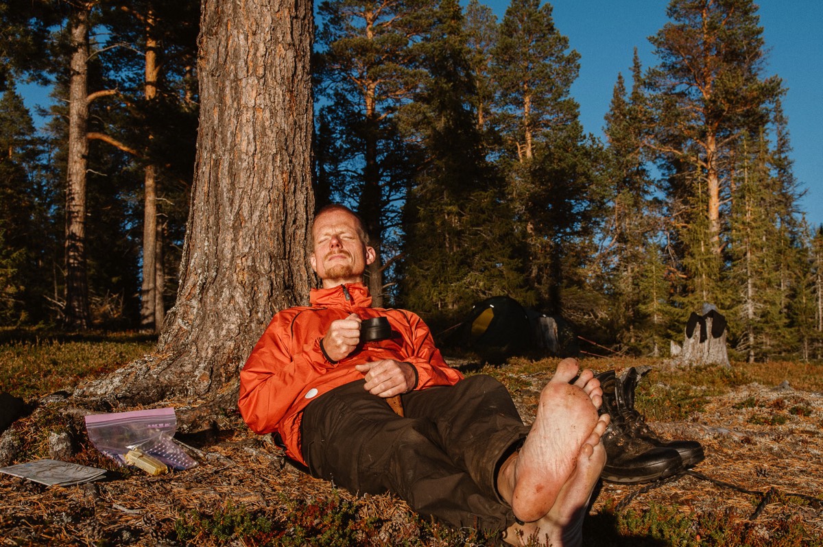 Bröllopsfotograf Johan Lindqvist sitter lutad mot en tall i fjällnära skog och dricker kaffe. Han blunder och njuter av solen och har bara fötter.