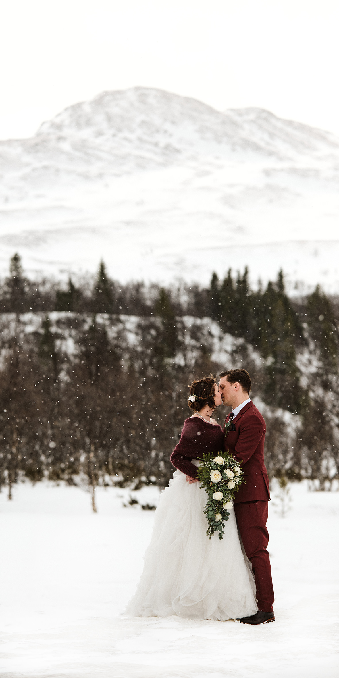 Bröllopsfotografering i fjällen - vinterbröllop - brudpar pussas i snöväder framför ett fjäll